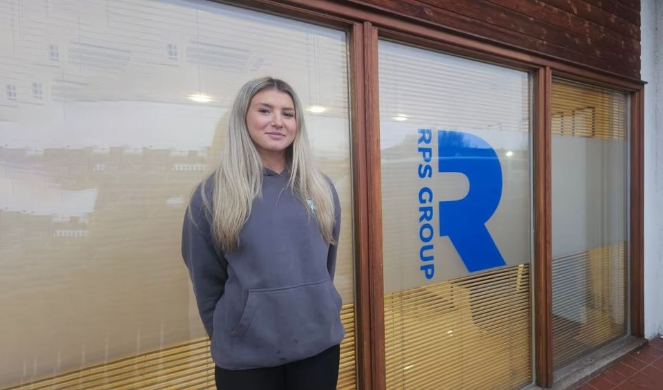 The image shows a person standing in front of a building with glass windows featuring the "RPS Group" logo.